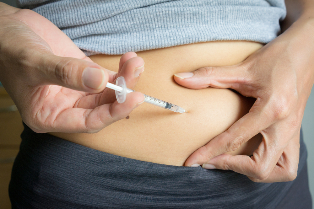 person injecting themselves in abdomen with needle and syringe