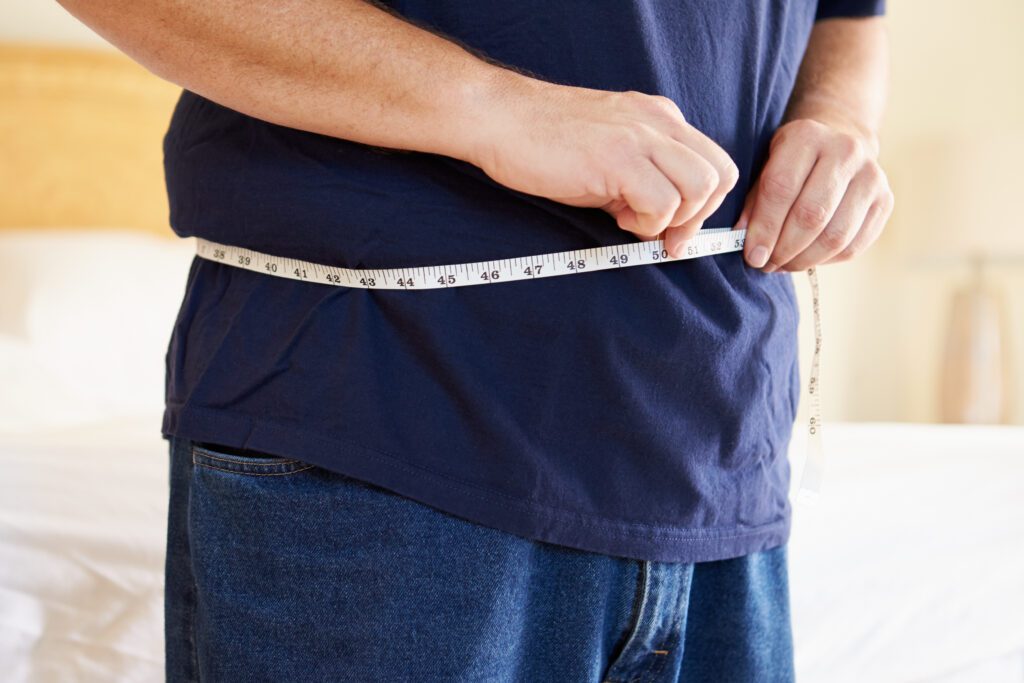 man with tape measure measuring his waist size