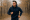 young man jogging outdoors in a navy hoodie on a wooded path.