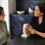 2026 08 mirabilemdcom img facial anatomy education v1 mirabile md - provider using a facial anatomy model to explain treatment areas during a patient consultation.