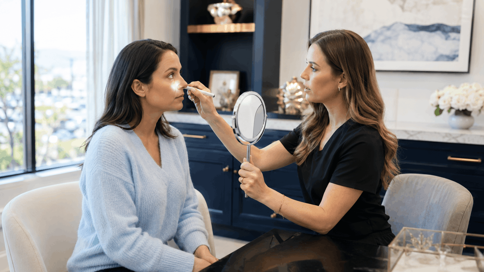 provider evaluating a patient's facial features with a handheld mirror during an aesthetic consultation.