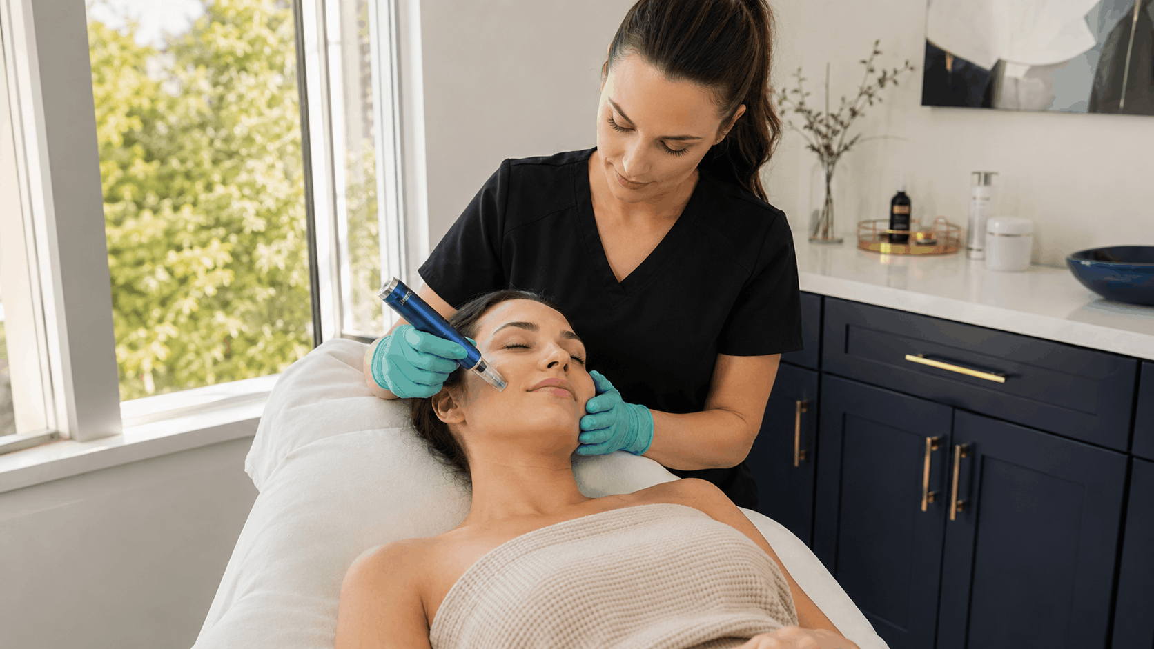2026 08 mirabilemdcom img hydrafacial treatment v1 mirabile md - provider performing a hydrafacial treatment on a patient in a comfortable treatment room.
