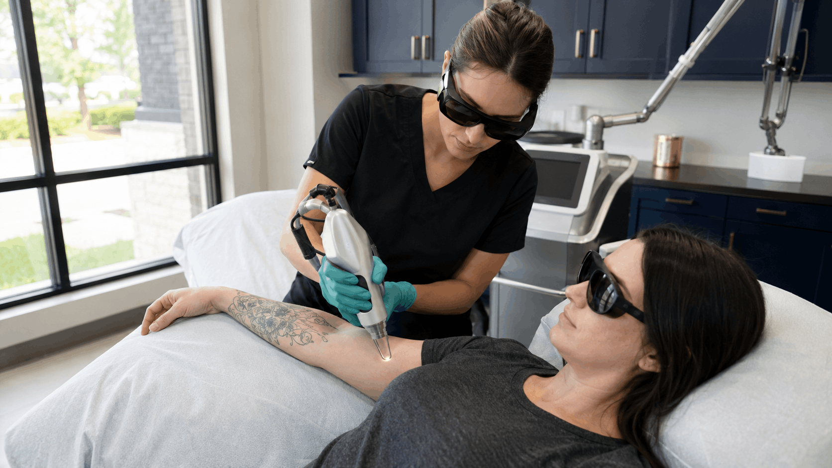 2026 08 mirabilemdcom img laser tattoo removal v1 mirabile md - provider using a laser device to treat a patient's tattooed forearm while both wear protective eyewear.