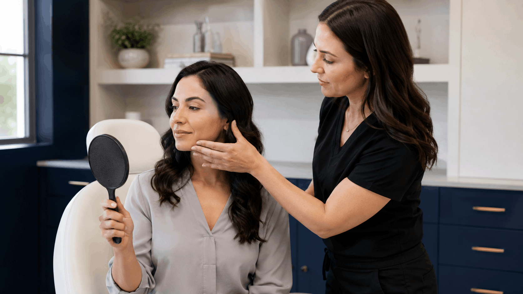 provider assessing a patient’s face while the patient looks into a handheld mirror.